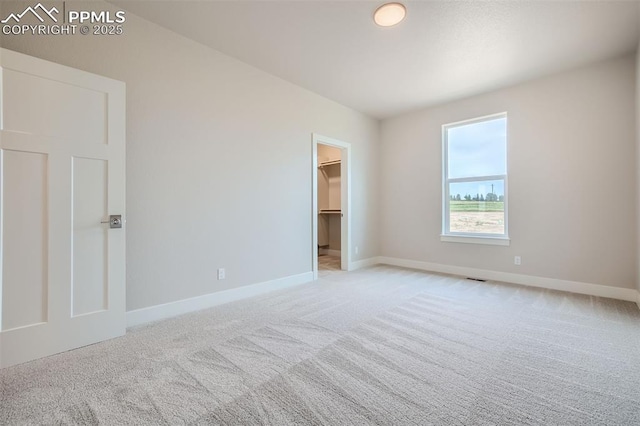 unfurnished bedroom featuring light colored carpet and a walk in closet