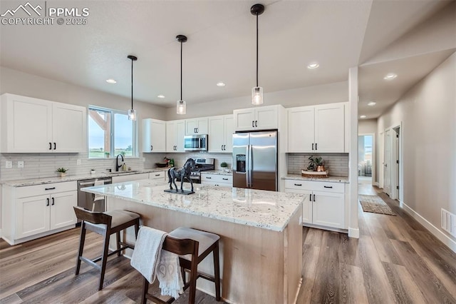 kitchen featuring a kitchen island, appliances with stainless steel finishes, decorative light fixtures, sink, and white cabinets