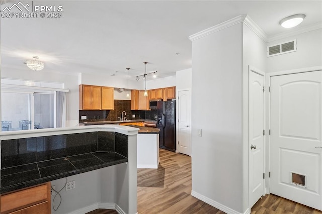 kitchen with sink, hanging light fixtures, wood-type flooring, black fridge, and kitchen peninsula