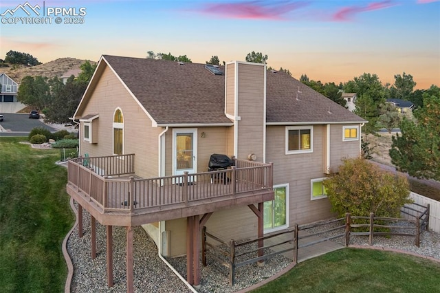 back house at dusk with a wooden deck, a balcony, and a yard