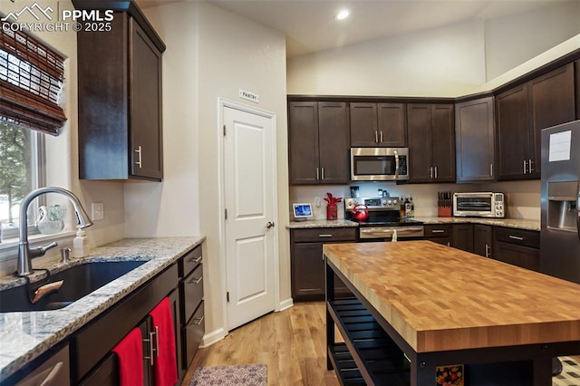 kitchen with sink, light stone counters, light hardwood / wood-style floors, stainless steel appliances, and dark brown cabinets