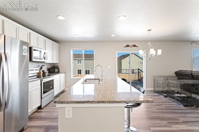 kitchen with sink, white cabinetry, decorative light fixtures, appliances with stainless steel finishes, and a kitchen island with sink