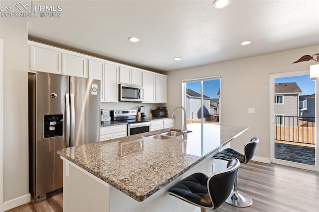 kitchen with stainless steel appliances, a center island with sink, and white cabinets