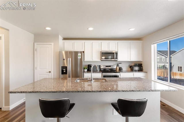 kitchen featuring white cabinetry, sink, stainless steel appliances, dark wood-type flooring, and a center island with sink