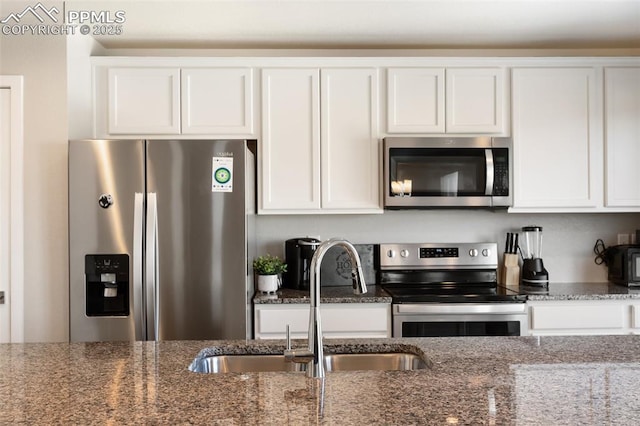 kitchen featuring sink, dark stone counters, white cabinets, and appliances with stainless steel finishes