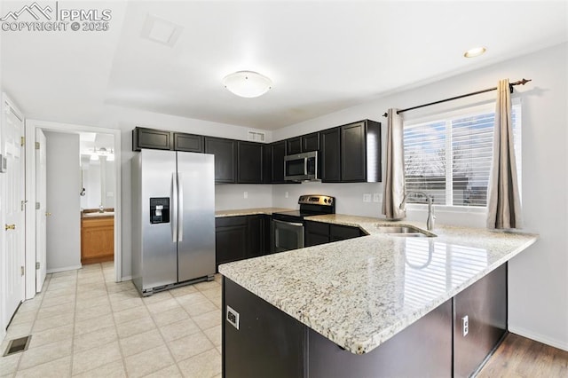 kitchen with appliances with stainless steel finishes, kitchen peninsula, sink, and light stone countertops