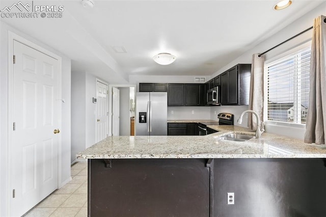 kitchen with light tile patterned floors, sink, appliances with stainless steel finishes, light stone countertops, and kitchen peninsula