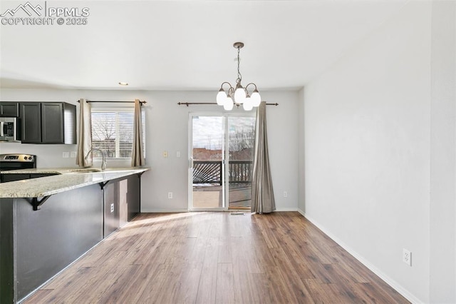 kitchen with appliances with stainless steel finishes, pendant lighting, a kitchen bar, light stone counters, and kitchen peninsula