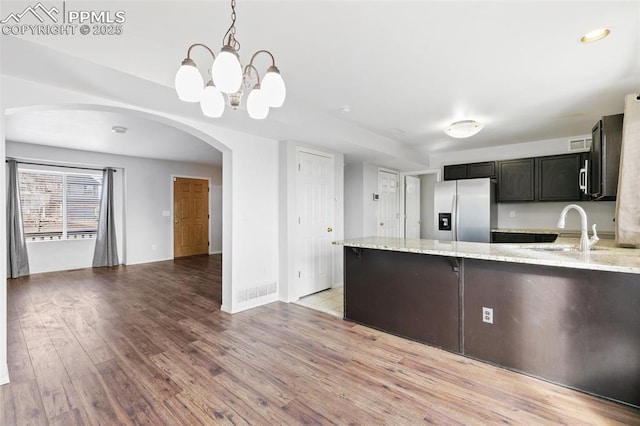 kitchen with sink, stainless steel fridge, hanging light fixtures, light stone counters, and light hardwood / wood-style floors