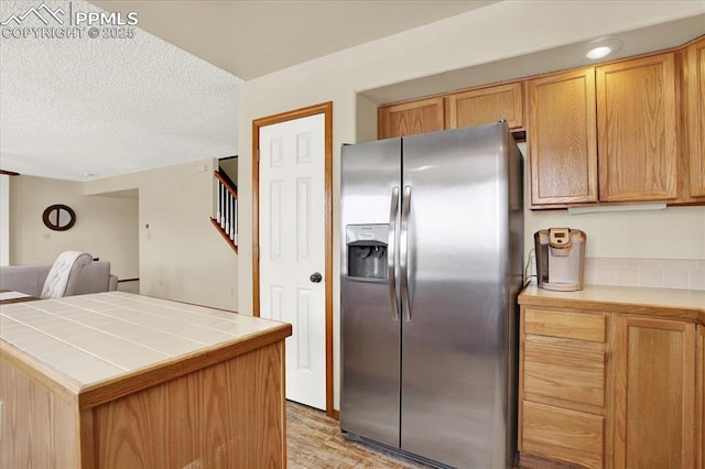 kitchen featuring light hardwood / wood-style flooring, tile countertops, a textured ceiling, and stainless steel fridge with ice dispenser