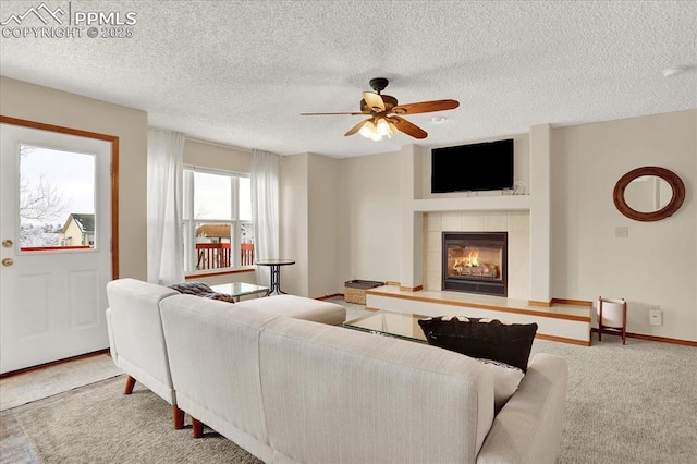 living room with a tiled fireplace, a textured ceiling, ceiling fan, and carpet