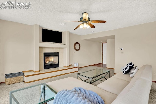 carpeted living room with ceiling fan, a tile fireplace, and a textured ceiling