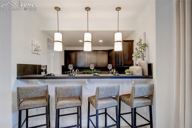 kitchen featuring dark brown cabinetry, a kitchen breakfast bar, kitchen peninsula, and hanging light fixtures