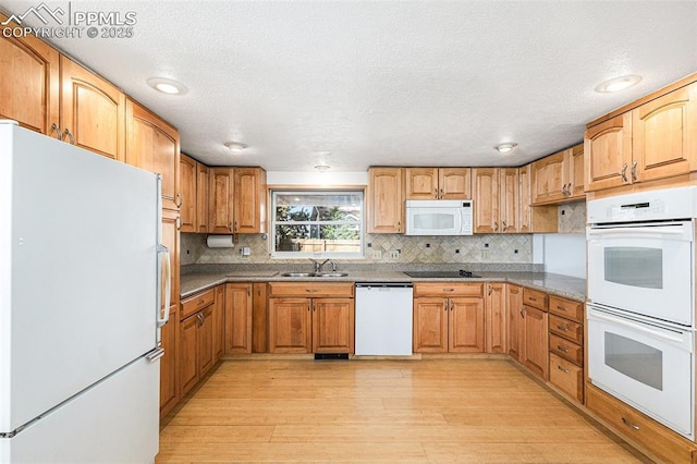 kitchen with tasteful backsplash, sink, white appliances, light hardwood / wood-style floors, and a textured ceiling