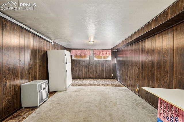 basement featuring a textured ceiling, carpet floors, white fridge, and wood walls