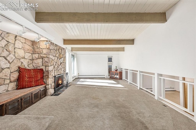 unfurnished living room with a stone fireplace, rail lighting, carpet flooring, baseboard heating, and beam ceiling