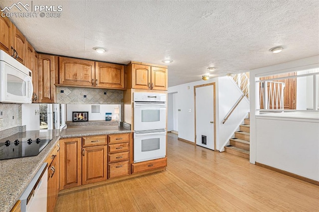 kitchen with light wood-type flooring, a wealth of natural light, a textured ceiling, and white appliances