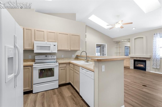 kitchen with vaulted ceiling with skylight, wood-type flooring, sink, kitchen peninsula, and white appliances