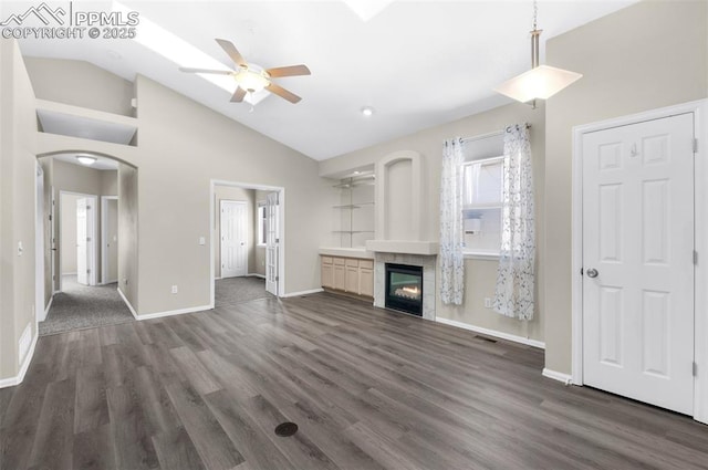 unfurnished living room with a tiled fireplace, dark wood-type flooring, high vaulted ceiling, and ceiling fan