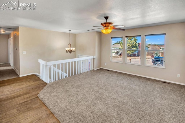 spare room with a textured ceiling, ceiling fan with notable chandelier, wood finished floors, visible vents, and baseboards