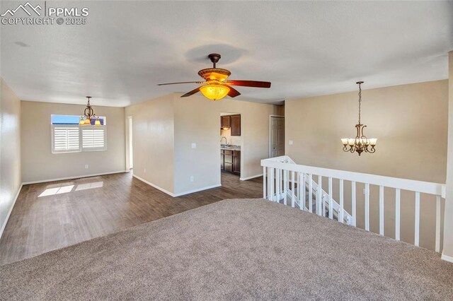 spare room with baseboards, dark wood-style flooring, and ceiling fan with notable chandelier