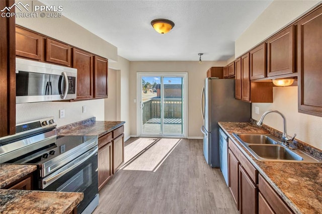 kitchen featuring baseboards, dark countertops, appliances with stainless steel finishes, light wood-style floors, and a sink