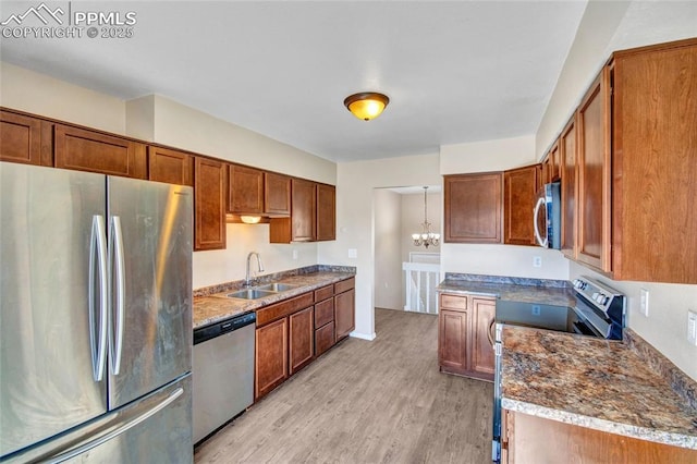 kitchen with a chandelier, stainless steel appliances, a sink, light wood-type flooring, and brown cabinets