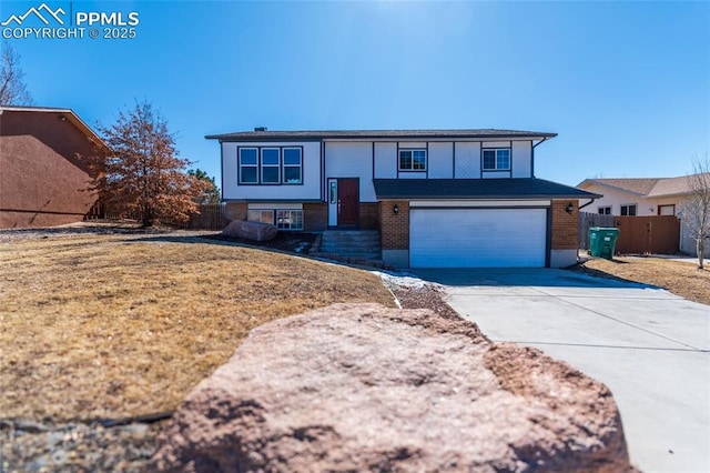 bi-level home with concrete driveway, brick siding, an attached garage, and fence