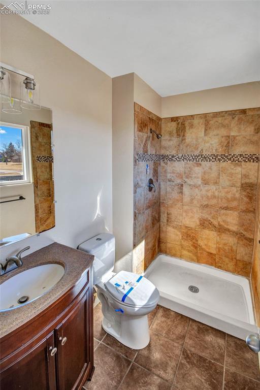 full bathroom with toilet, tile patterned flooring, tiled shower, and vanity