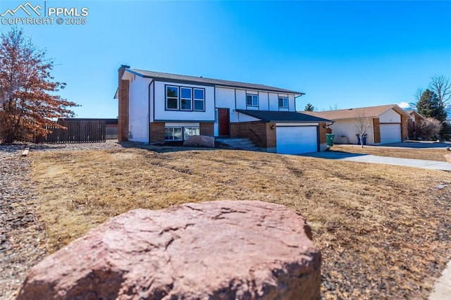 bi-level home featuring an attached garage, brick siding, fence, driveway, and a chimney