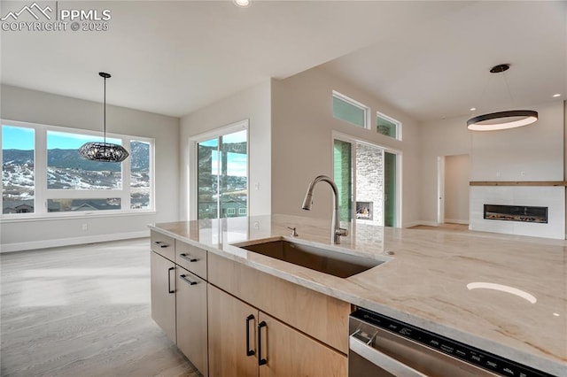 kitchen featuring decorative light fixtures, dishwasher, sink, light stone countertops, and light brown cabinets