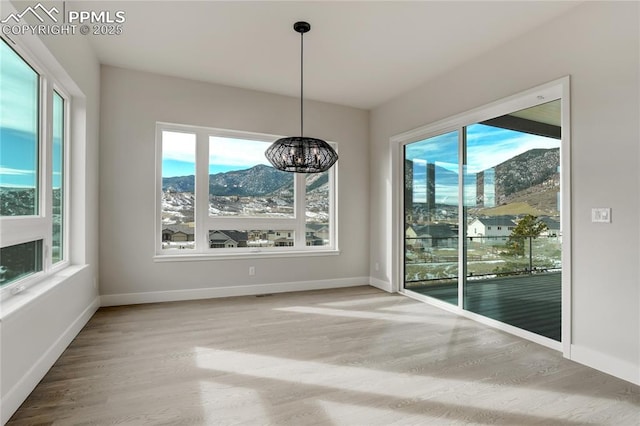 unfurnished dining area with an inviting chandelier, a mountain view, hardwood / wood-style floors, and a wealth of natural light