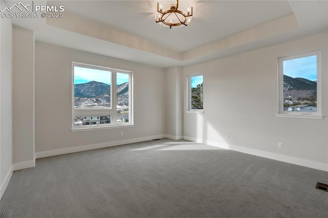 spare room with a tray ceiling, a chandelier, and carpet flooring