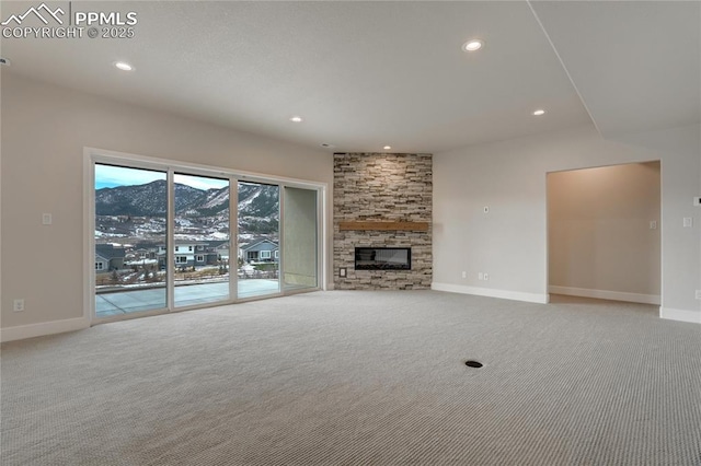 unfurnished living room featuring a stone fireplace, a mountain view, and light carpet