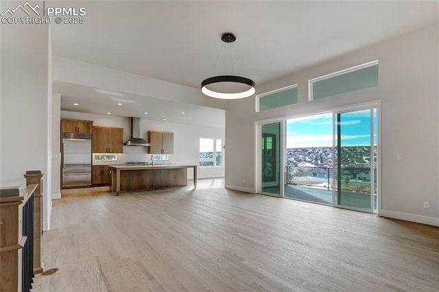 kitchen with light hardwood / wood-style flooring, hanging light fixtures, a center island, stainless steel built in refrigerator, and wall chimney exhaust hood