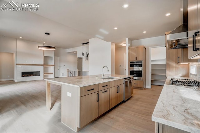 kitchen featuring sink, appliances with stainless steel finishes, a spacious island, light stone counters, and decorative light fixtures