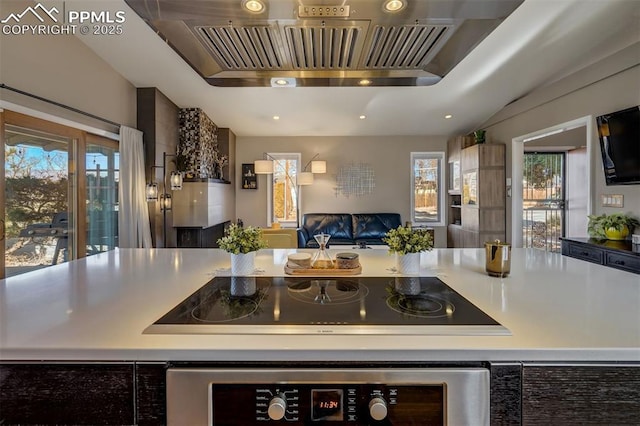 kitchen with black electric cooktop, a healthy amount of sunlight, premium range hood, and wall oven