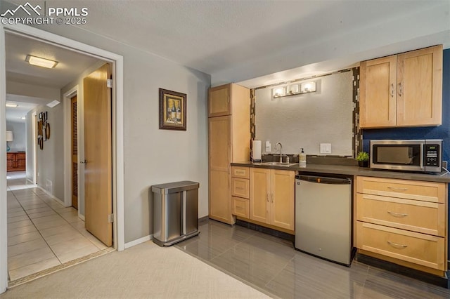 kitchen with dishwashing machine, sink, tile patterned flooring, and light brown cabinetry