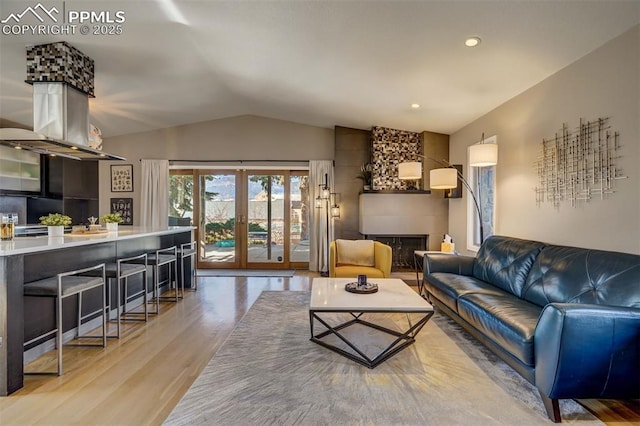 living room with lofted ceiling, a large fireplace, french doors, and light wood-type flooring