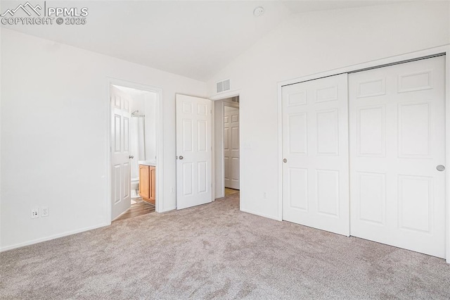 unfurnished bedroom featuring a closet, connected bathroom, vaulted ceiling, and light carpet