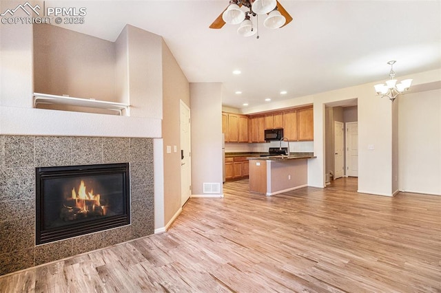 interior space featuring hanging light fixtures, light wood-type flooring, a kitchen breakfast bar, a tile fireplace, and ceiling fan with notable chandelier