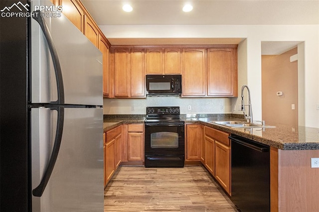 kitchen with sink, black appliances, kitchen peninsula, dark stone counters, and light wood-type flooring