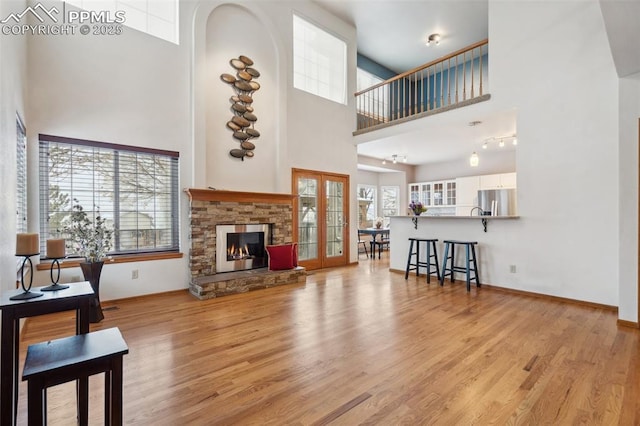 living room with french doors, a towering ceiling, a stone fireplace, and light hardwood / wood-style floors