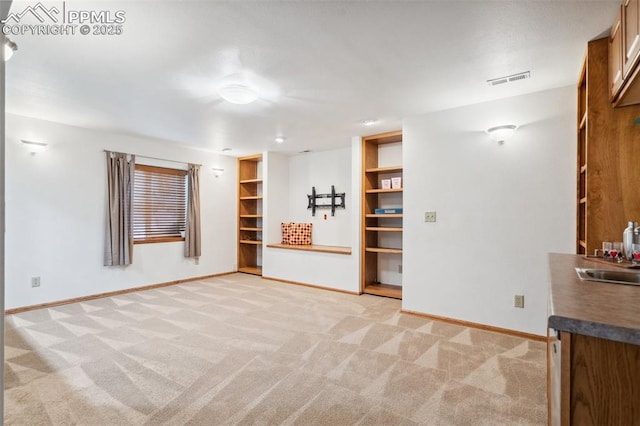 unfurnished living room featuring sink, light carpet, and built in features