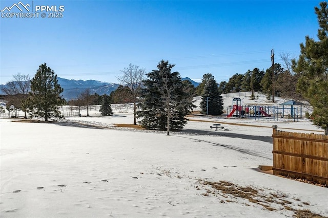 yard layered in snow featuring a mountain view and a playground