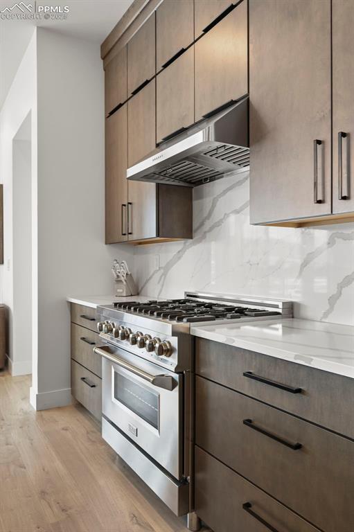 kitchen featuring stainless steel range, light stone countertops, light hardwood / wood-style floors, and decorative backsplash