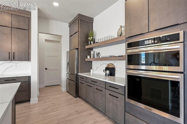 kitchen with appliances with stainless steel finishes, dark brown cabinets, light hardwood / wood-style floors, and decorative backsplash