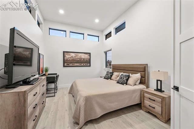 bedroom with a towering ceiling and light hardwood / wood-style floors