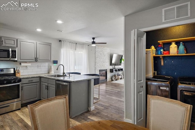 kitchen with sink, light wood-type flooring, appliances with stainless steel finishes, gray cabinets, and kitchen peninsula