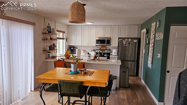 kitchen with stainless steel appliances, white cabinetry, hardwood / wood-style flooring, and decorative backsplash